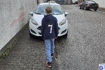 Kind vor einem am Bürgersteig parkenden Auto