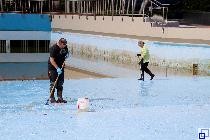 Zwei Mitarbeiter schrubben den Schwimmbeckenboden