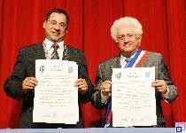 Das Bild zeigt die Bürgermeister Jürgen Kappenstein und Marc Goua mit den unterzeichneten Verträgen