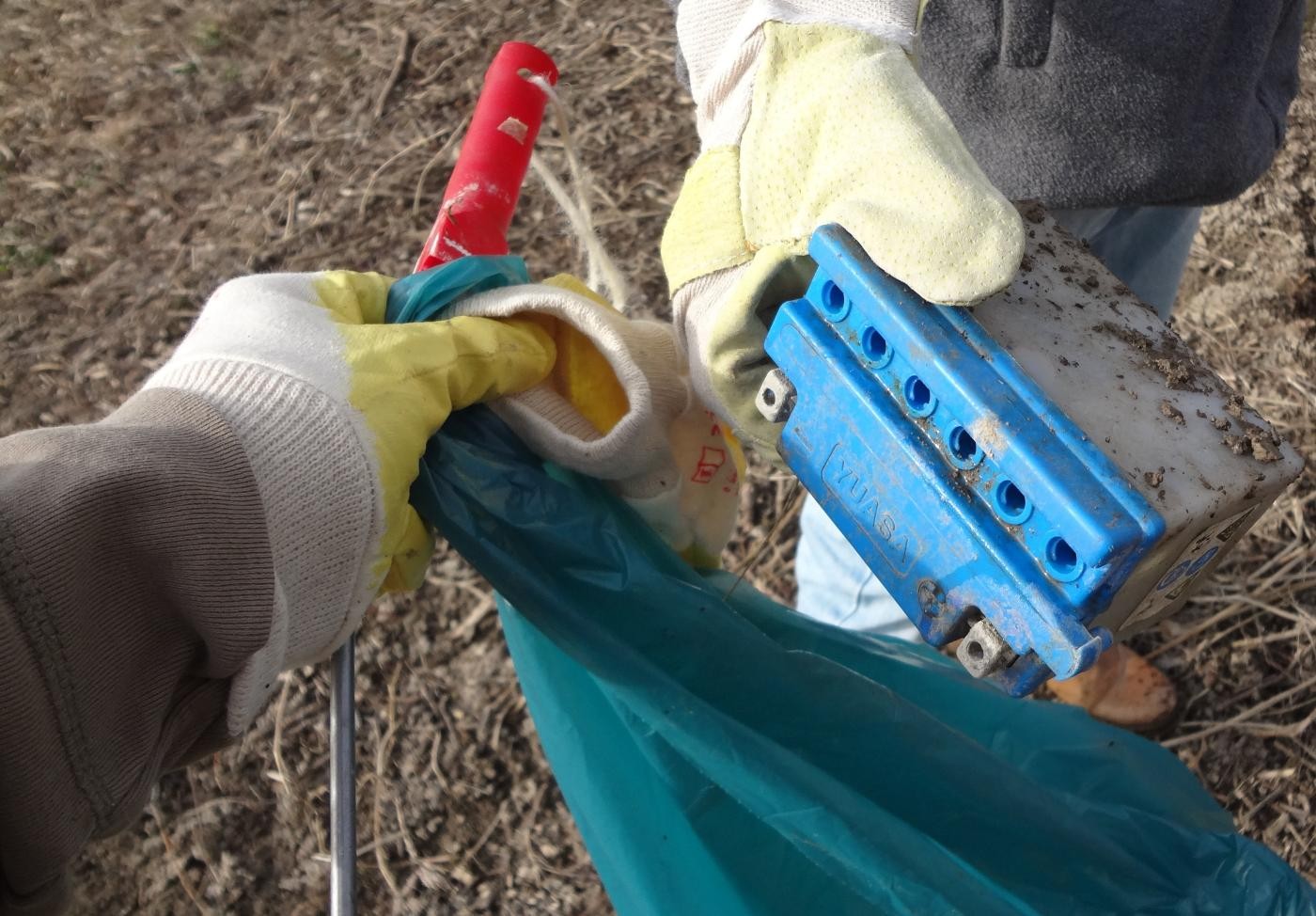 Zwei Hände: eine Hand hält den Müllsack, die andere eine gefundene Autobatterie